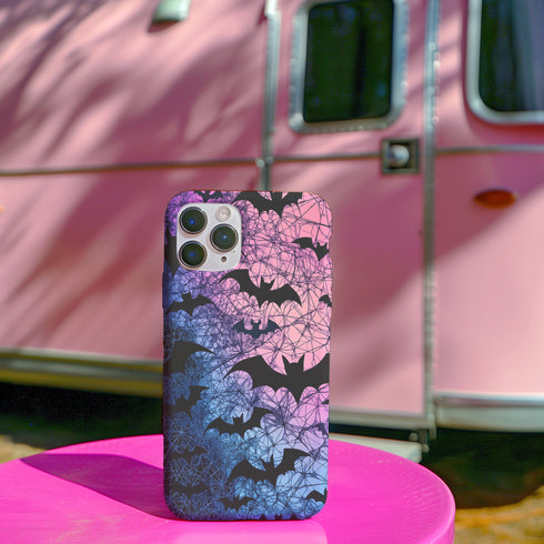 A pastel gothic phone case featuring black bat silhouettes over a gradient pink-to-blue ombré background with web-like detailing. Available for iPhone, Samsung, and Google Pixel models in matte or glossy finishes with dual-layer protection.