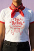 White women's cropped ringer t-shirt with bright red trim on the collar and sleeves. The chest features a cute kawaii graphic in red and soft pink. The text reads "Tax the Rich" in a retro serif font, followed by "Feed the Poor" and "Pet the Cats" in script and sans-serif. Surrounding the text are hearts, sparkles, and flowers. At the bottom, a happy line-art cat with closed smiling eyes raises its paws in the air. The style is flat, 2D, and anime-inspired.