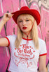 White women's cropped ringer t-shirt with bright red trim on the collar and sleeves. The chest features a cute kawaii graphic in red and soft pink. The text reads "Tax the Rich" in a retro serif font, followed by "Feed the Poor" and "Pet the Cats" in script and sans-serif. Surrounding the text are hearts, sparkles, and flowers. At the bottom, a happy line-art cat with closed smiling eyes raises its paws in the air. The style is flat, 2D, and anime-inspired.