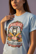 A short sleeve unisex crewneck t-shirt featuring a vintage style emblem graphic centered on the chest. The design features a red banner reading BAKE SALE above a black guillotine. Two crossed wooden rolling pins sit below the guillotine, above a layered pink and white cake with a cherry. The graphic is flanked by pink flowers, cherries, and stacks of gold coins. A bottom banner reads FOR THE GUILLOTINE FUND EST. WHENEVER THEY GOT TOO GREEDY. The shirt comes in light pink, cream, and blue.
