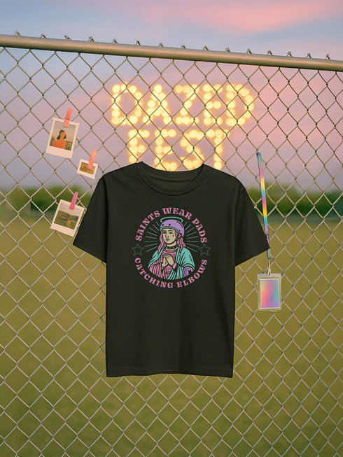 Black unisex t-shirt with bold graphic that reads "Saints Wear Pads Catching Elbows" surrounding a pastel saint figure wearing a roller skate helmet and protective pads. The design mimics embroidery in a retro tattoo-inspired art style. Available in sizes S to 3XL, this skate tee is soft, comfortable, and perfect for roller derby lovers, punk skaters, and feminist fashion fans. Great birthday or skate party gift idea.