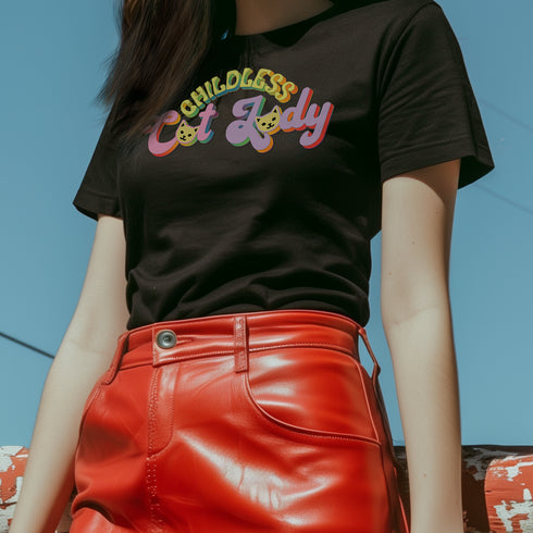 An election 2024 t-shirt with a colorful retro-style graphic that reads "Childless Cat Lady" across the chest. The text is in a playful, curvy font with each word in a different color - "Childless" in yellow-green, "Cat" in pink, and "Lady" in purple. Small cat face icons are incorporated into the letters 'a' in "Cat" and "Lady".