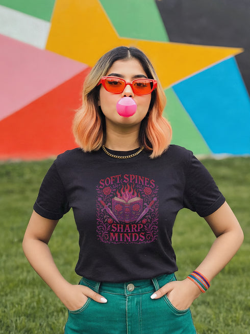 Unisex black t-shirt featuring a faux-embroidered design of a flaming open book with roses and dual daggers, surrounded by gothic flourishes and text that reads “Soft Spines, Sharp Minds.” Printed in vivid pink and red tones with ornate detailing. Available in 100% cotton or vintage-feel cotton/poly blend, sizes S–3XL. Perfect for goth book lovers, alt fashion fans, and anyone who blends brains with rebellion.
