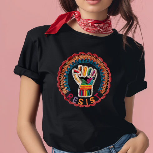 Black short-sleeve t-shirt featuring a bold embroidered design centered on the chest. The design showcases a raised fist wrapped in multicolored thread, symbolizing strength and resistance. Surrounding the fist is a circular embroidered border with intricate, colorful stitching in shades of red, orange, blue, and yellow, creating a striking contrast against the black fabric. Below the fist, the word "RESIST" is embroidered in capital letters using a gradient of warm-toned thread. The t-shirt has a classic c