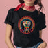 Black short-sleeve t-shirt featuring a bold embroidered design centered on the chest. The design showcases a raised fist wrapped in multicolored thread, symbolizing strength and resistance. Surrounding the fist is a circular embroidered border with intricate, colorful stitching in shades of red, orange, blue, and yellow, creating a striking contrast against the black fabric. Below the fist, the word "RESIST" is embroidered in capital letters using a gradient of warm-toned thread. The t-shirt has a classic c