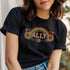 Black unisex t-shirt with "ALLY" in gold lettering under a rainbow arch, flanked by two large sunflower designs. LGBTQ+ pride ally shirt with folk art-inspired elements, available in cotton-poly blend, sizes S-3XL.