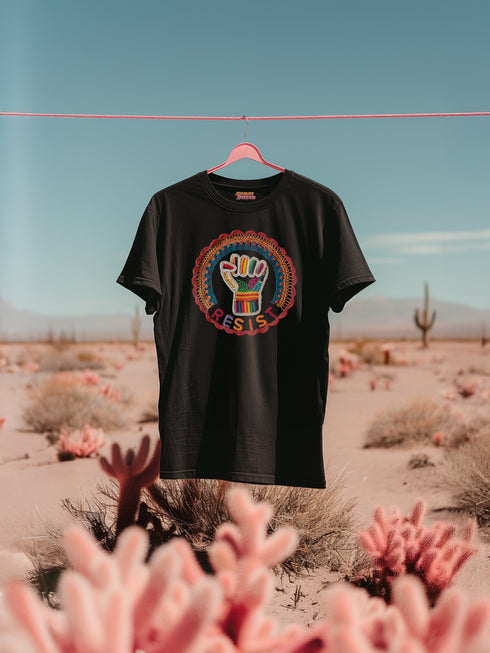 Black short-sleeve t-shirt featuring a bold embroidered design centered on the chest. The design showcases a raised fist wrapped in multicolored thread, symbolizing strength and resistance. Surrounding the fist is a circular embroidered border with intricate, colorful stitching in shades of red, orange, blue, and yellow, creating a striking contrast against the black fabric. Below the fist, the word "RESIST" is embroidered in capital letters using a gradient of warm-toned thread. The t-shirt has a classic c