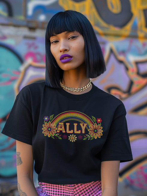 Black unisex t-shirt with "ALLY" in gold lettering under a rainbow arch, flanked by two large sunflower designs. LGBTQ+ pride ally shirt with folk art-inspired elements, available in cotton-poly blend, sizes S-3XL.