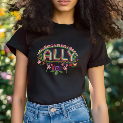 Black t-shirt featuring "ALLY" in gold letters protected by a rainbow arch and flanked by two sunflowers. LGBTQ+ pride ally shirt with colorful folk art-inspired design, available in cotton-poly blend, sizes S-3XL.