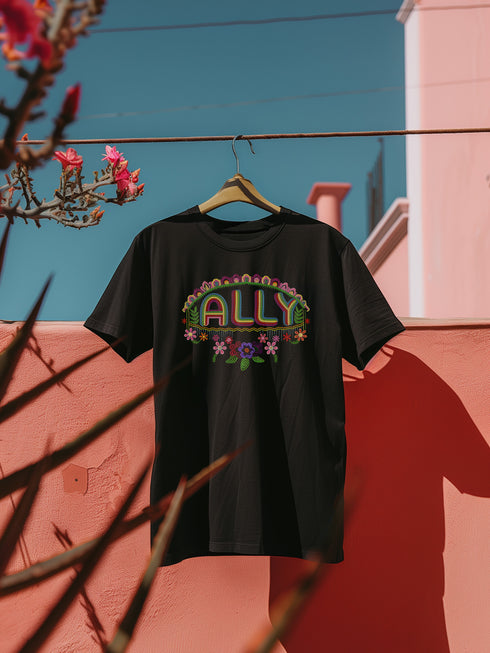 Black t-shirt featuring "ALLY" in gold letters protected by a rainbow arch and flanked by two sunflowers. LGBTQ+ pride ally shirt with colorful folk art-inspired design, available in cotton-poly blend, sizes S-3XL.