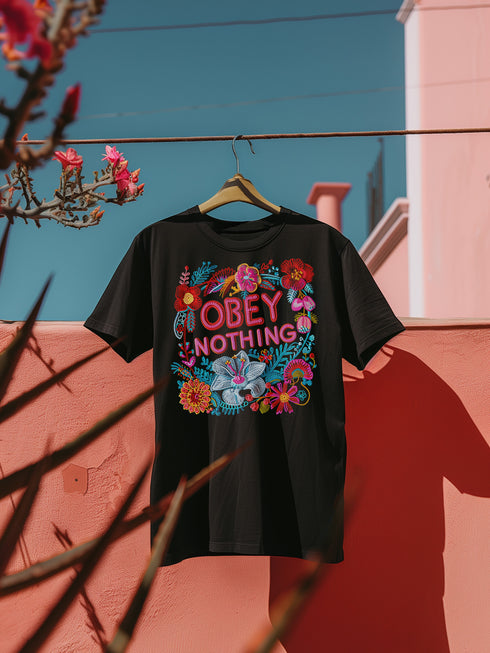 Black activist T-shirt with a floral embroidered-style design and the words “Obey Nothing” in bold, bright lettering.