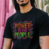 Black unisex t-shirt with colorful "POWER TO THE PEOPLE" text design in orange, pink, and green lettering surrounded by swirling psychedelic rainbow border.