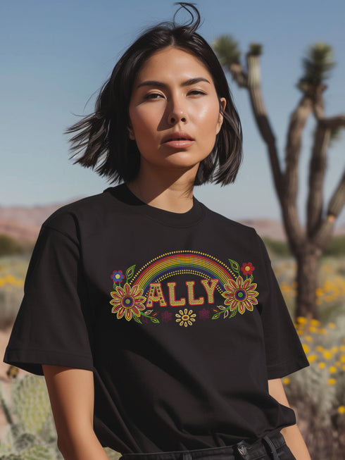 Black unisex t-shirt with "ALLY" in gold lettering under a rainbow arch, flanked by two large sunflower designs. LGBTQ+ pride ally shirt with folk art-inspired elements, available in cotton-poly blend, sizes S-3XL.