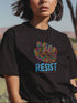 Black t-shirt with vibrant multicolored patterned raised fist graphic and blue "RESIST" text underneath. Rainbow activist protest shirt with psychedelic design elements on cotton-polyester blend.