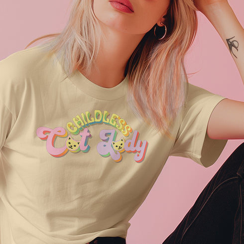 An election 2024 t-shirt with a colorful retro-style graphic that reads "Childless Cat Lady" across the chest. The text is in a playful, curvy font with each word in a different color - "Childless" in yellow-green, "Cat" in pink, and "Lady" in purple. Small cat face icons are incorporated into the letters 'a' in "Cat" and "Lady".
