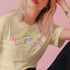 An election 2024 t-shirt with a colorful retro-style graphic that reads "Childless Cat Lady" across the chest. The text is in a playful, curvy font with each word in a different color - "Childless" in yellow-green, "Cat" in pink, and "Lady" in purple. Small cat face icons are incorporated into the letters 'a' in "Cat" and "Lady".