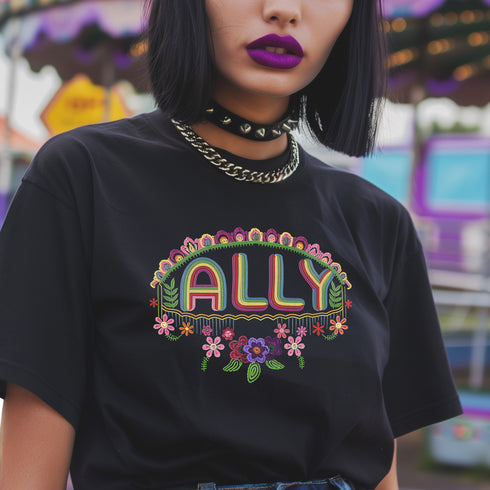 Black t-shirt featuring "ALLY" in gold letters protected by a rainbow arch and flanked by two sunflowers. LGBTQ+ pride ally shirt with colorful folk art-inspired design, available in cotton-poly blend, sizes S-3XL.