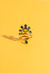 A close-up of a Berber Gripoix Wrap Ring in brass and enamel, featuring abstract teal and amber shapes on a yellow background. The ring’s sculptural wrap design and artistic details are highlighted in bright, natural light. Handmade statement jewelry by Honey Dazed.