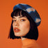 A wool beret with a hand-dyed pattern in deep indigo blue and white. The beret has a soft, rounded shape with a small fabric loop on top, creating a classic, French-inspired look. The pattern features irregular, organic shapes resembling a tie-dye effect, giving it a modern, artistic vibe.