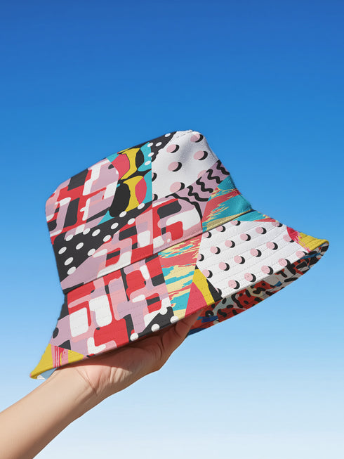 A reversible 90s-inspired bucket hat with two maximalist designs. One side showcases a colorful collage of polka dots and abstract patchwork shapes in vibrant reds, yellows, greens, and blues, evoking a playful retro feel. The opposite side features a contrasting blue-toned leopard print with geometric accents, adding an edgy streetwear flair. The hat has a soft linen-textured polyester fabric that’s lightweight, moisture-wicking, and breathable.