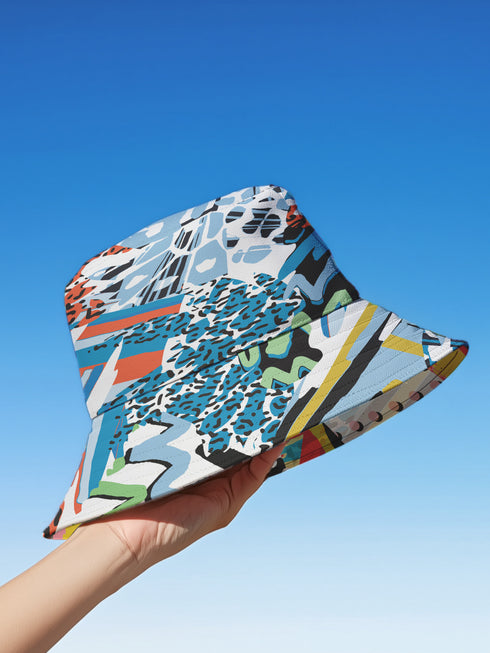 A reversible 90s-inspired bucket hat with two maximalist designs. One side showcases a colorful collage of polka dots and abstract patchwork shapes in vibrant reds, yellows, greens, and blues, evoking a playful retro feel. The opposite side features a contrasting blue-toned leopard print with geometric accents, adding an edgy streetwear flair. The hat has a soft linen-textured polyester fabric that’s lightweight, moisture-wicking, and breathable.