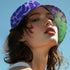 Reversible unisex bucket hat featuring two distinct designs - one side showcases a vibrant floral pop art pattern with purple, pink, green and blue splashes and organic flower motifs, while the reverse side displays a purple giraffe print pattern with dark purple giraffe spots on a light purple background. Made from 100% polyester with textured linen feel, this moisture-wicking and breathable hat is available in XS, S/M, and L/XL sizes for ultimate style versatility.
