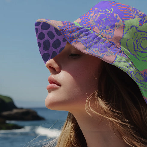 Reversible unisex bucket hat featuring two distinct designs - one side showcases a vibrant floral pop art pattern with purple, pink, green and blue splashes and organic flower motifs, while the reverse side displays a purple giraffe print pattern with dark purple giraffe spots on a light purple background. Made from 100% polyester with textured linen feel, this moisture-wicking and breathable hat is available in XS, S/M, and L/XL sizes for ultimate style versatility.