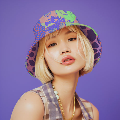 Reversible unisex bucket hat featuring two distinct designs - one side showcases a vibrant floral pop art pattern with purple, pink, green and blue splashes and organic flower motifs, while the reverse side displays a purple giraffe print pattern with dark purple giraffe spots on a light purple background. Made from 100% polyester with textured linen feel, this moisture-wicking and breathable hat is available in XS, S/M, and L/XL sizes for ultimate style versatility.
