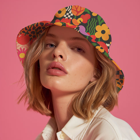 a reversible bucket hat. The visible side features a maximalist 70s-inspired pattern with bold orange, purple, and yellow abstract flowers on a black background with white checkerboard accents. The hat is made of a breathable, linen-feel polyester. The reverse side, hinted at on the brim's underside, has a vibrant Y2K psychedelic print with leopard spots and tropical fruit. This funky, colorful sun hat is a perfect dopamine dressing accessory for festival fashion.