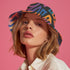 Reversible bucket hat with a bold all-over psychedelic tiger stripe print in pink, blue, yellow, and black; made of moisture-wicking polyester with a linen-texture feel; available in sizes XS, S/M, and L/XL; features two different sides with unique patterns.