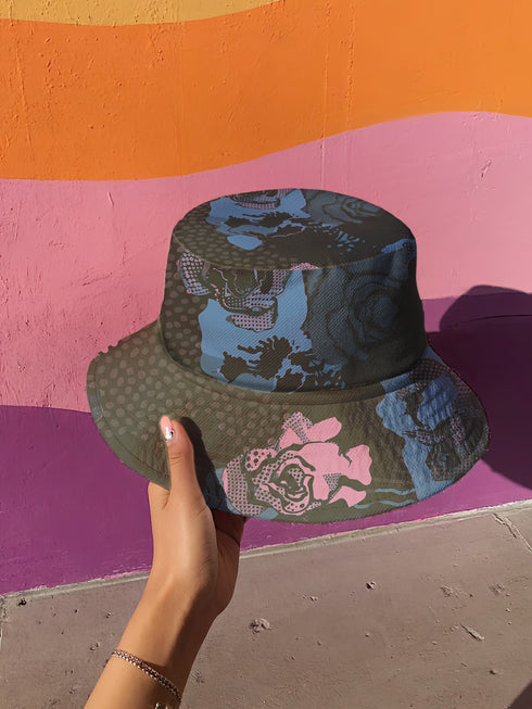 Abstract pop art floral bucket hat featuring a vibrant and bold artistic design with colorful floral motifs in bright pink, orange, yellow, blue, and black tones. The design showcases oversized abstract flowers, coral-like organic shapes, and decorative patterns with dots and stripes in a contemporary pop art style. Made from 100% polyester with textured linen feel, this moisture-wicking and breathable unisex hat is available in XS, S/M, and L/XL sizes, perfect for festivals, streetwear, and artistic fashio