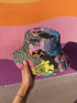 Abstract pop art floral bucket hat featuring a vibrant and bold artistic design with colorful floral motifs in bright pink, orange, yellow, blue, and black tones. The design showcases oversized abstract flowers, coral-like organic shapes, and decorative patterns with dots and stripes in a contemporary pop art style. Made from 100% polyester with textured linen feel, this moisture-wicking and breathable unisex hat is available in XS, S/M, and L/XL sizes, perfect for festivals, streetwear, and artistic fashio