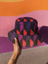 Reversible unisex bucket hat featuring two distinct geometric designs - one side showcases a bold abstract pattern with angular shapes in vibrant purple, pink, red, and black creating dynamic geometric forms and diamond-like structures, while the reverse side displays a contemporary abstract composition with curved organic shapes, linear textures, and color-blocking in purple, red, and black tones. Made from 100% polyester with textured linen feel, this moisture-wicking and breathable hat is available in XS