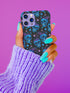 Black phone case featuring bright electric blue skulls with purple cherry stems and colorful stars scattered throughout the pattern. Gothic yet playful design.