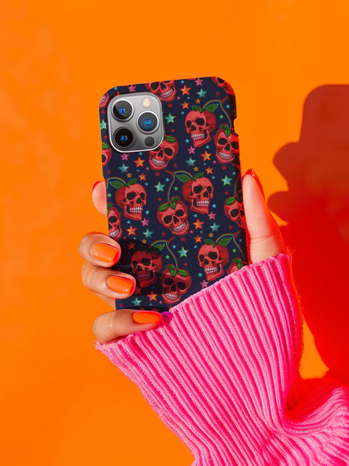 Phone case featuring vibrant red apple skulls with green stems and multicolored stars on navy background. Gothic alternative design with bright colorful accents.