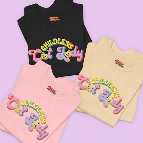 An election 2024 t-shirt with a colorful retro-style graphic that reads "Childless Cat Lady" across the chest. The text is in a playful, curvy font with each word in a different color - "Childless" in yellow-green, "Cat" in pink, and "Lady" in purple. Small cat face icons are incorporated into the letters 'a' in "Cat" and "Lady".