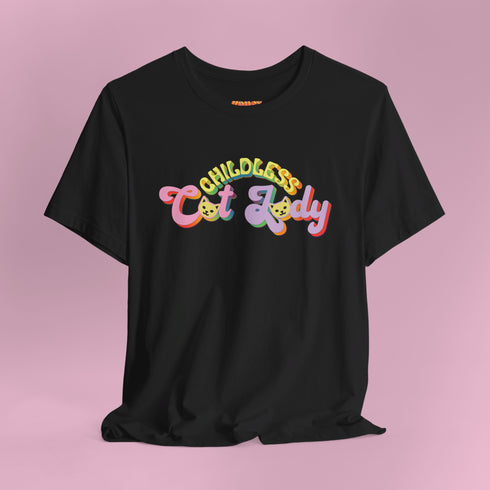An election 2024 t-shirt with a colorful retro-style graphic that reads "Childless Cat Lady" across the chest. The text is in a playful, curvy font with each word in a different color - "Childless" in yellow-green, "Cat" in pink, and "Lady" in purple. Small cat face icons are incorporated into the letters 'a' in "Cat" and "Lady".