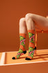 Mid-calf crew sock with a bold retro 70s maximalist botanical print. A deep green base is packed with golden yellow fern-like leaves, pink folk-style flowers with red centers, and clusters of round red and pink berries. Orange and red shell motifs with wavy stripes band the cuff and lower sock. The toe and heel are solid black. The fabric is a soft, stretchy printed knit, made as a one-size unisex statement sock for maximalist and dopamine dressing looks.