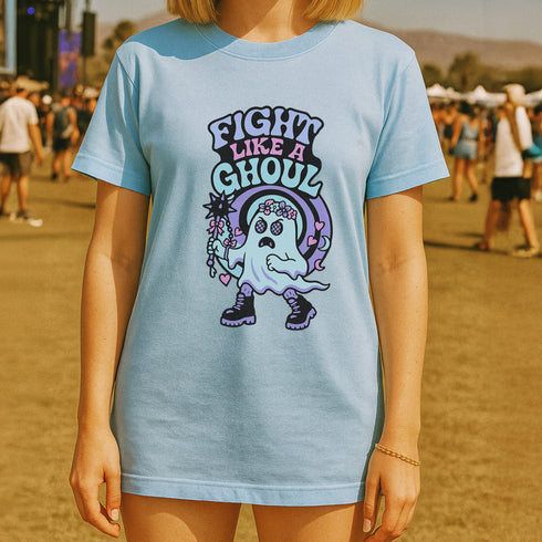 Unisex Comfort Colors 1717 t-shirt featuring a front print of a cute gothic ghost holding a mace wand with text reading "Fight Like A Ghoul." The ghost has floral details, combat boots, and pastel accents. Made of soft-washed, 100% ring-spun cotton with garment-dyed fabric and seamless tubular knit construction. Available in sizes S to 4XL.