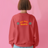 A Christmas sweatshirt featuring a playful design with a cartoon Baphomet goat character wearing a Santa hat. The design includes the text "All Hail Santa" above the goat, with pentagrams in flames on either side. The goat is depicted in a meditative pose, adding a humorous and irreverent twist to holiday attire.