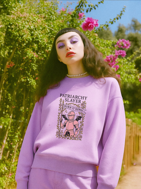 Comfort Colors garment-dyed sweatshirt featuring 'Patriarchy Slayer' design with pink armored knight holding sword and banner reading 'Burn It Down', surrounded by decorative floral border with roses and leaves. Made from 80% ring-spun cotton and 20% polyester with relaxed fit and rolled-forward shoulders. Available in lavender purple and seafoam green colorways, sizes S-3XL unisex, featuring sustainable made-to-order production with OEKO-TEX certified low-impact dyes and zero waste manufacturing process.