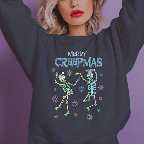 A dark green holiday sweatshirt featuring two dancing skeletons wearing Santa hats. The text "Merry Creepmas" is displayed above them in icy, drippy font. The design is surrounded by colorful snowflakes, blending spooky and festive elements for a fun, alternative holiday look.