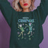 A dark green holiday sweatshirt featuring two dancing skeletons wearing Santa hats. The text "Merry Creepmas" is displayed above them in icy, drippy font. The design is surrounded by colorful snowflakes, blending spooky and festive elements for a fun, alternative holiday look.