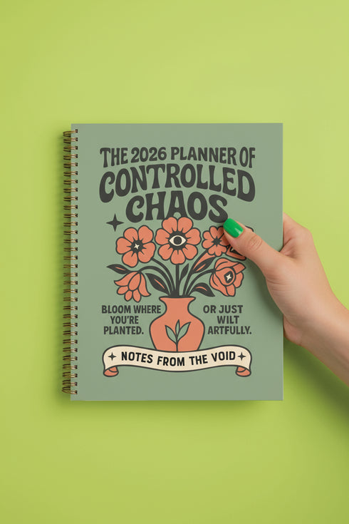 A sage green hardcover spiral planner for 2026 with the title "The 2026 Planner of Controlled Chaos" in a funky, retro 70s-style font. The cover features a groovy illustration of orange and pink flowers in a vase, with one flower depicted as an eyeball. The text reads "Bloom where you're planted. Or just wilt artfully." and "Notes from the Void." The planner has a gold metal wire-o binding. The back cover shows a decorative floral frame with a "Property Of" section