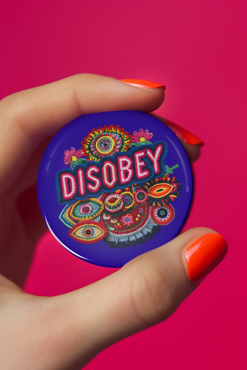 Stay Weird" black pinback button with pearl-effect lettering surrounded by folk art flowers in red and turquoise on a dark background.