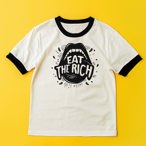 Heather gray ringer t-shirt with black contrast trim on the collar and sleeve cuffs. The front features a bold black graphic of an open mouth with the phrase "EAT THE RICH" in capital letters, integrated into the teeth. Surrounding the design are hand-drawn lines and accents, giving it a raw, punk-inspired aesthetic. The t-shirt has a vintage-inspired fit, made from soft cotton fabric with a slightly relaxed silhouette. The high-contrast black and gray design enhances the statement-making impact of the grap