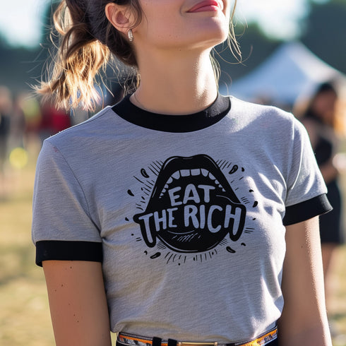 Heather gray ringer t-shirt with black contrast trim on the collar and sleeve cuffs. The front features a bold black graphic of an open mouth with the phrase "EAT THE RICH" in capital letters, integrated into the teeth. Surrounding the design are hand-drawn lines and accents, giving it a raw, punk-inspired aesthetic. The t-shirt has a vintage-inspired fit, made from soft cotton fabric with a slightly relaxed silhouette. The high-contrast black and gray design enhances the statement-making impact of the grap