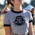 Heather gray ringer t-shirt with black contrast trim on the collar and sleeve cuffs. The front features a bold black graphic of an open mouth with the phrase "EAT THE RICH" in capital letters, integrated into the teeth. Surrounding the design are hand-drawn lines and accents, giving it a raw, punk-inspired aesthetic. The t-shirt has a vintage-inspired fit, made from soft cotton fabric with a slightly relaxed silhouette. The high-contrast black and gray design enhances the statement-making impact of the grap
