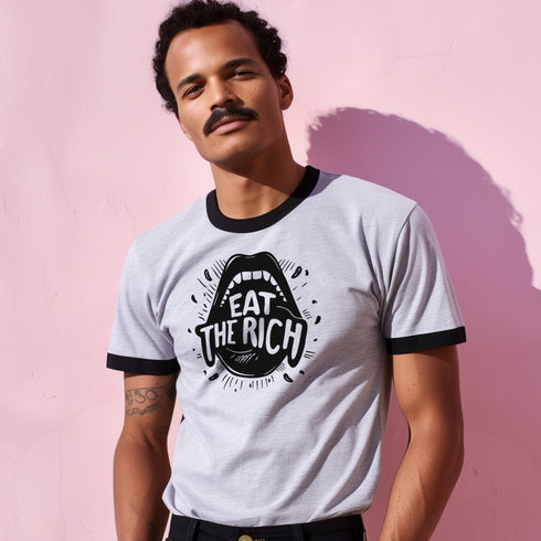 Heather gray ringer t-shirt with black contrast trim on the collar and sleeve cuffs. The front features a bold black graphic of an open mouth with the phrase "EAT THE RICH" in capital letters, integrated into the teeth. Surrounding the design are hand-drawn lines and accents, giving it a raw, punk-inspired aesthetic. The t-shirt has a vintage-inspired fit, made from soft cotton fabric with a slightly relaxed silhouette. The high-contrast black and gray design enhances the statement-making impact of the grap