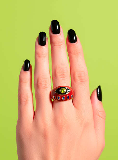 A red enamel Evil Eye Signet Ring with gold plating and zircon gemstone center, shown on a model’s hand with red nails. The ring’s symbolic design represents protection and empowerment. Bright yellow backdrop for modern maximalist appeal.